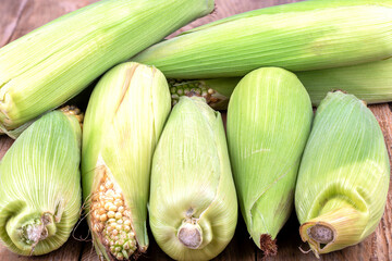 Cobs of unpeeled corn on a wooden table.