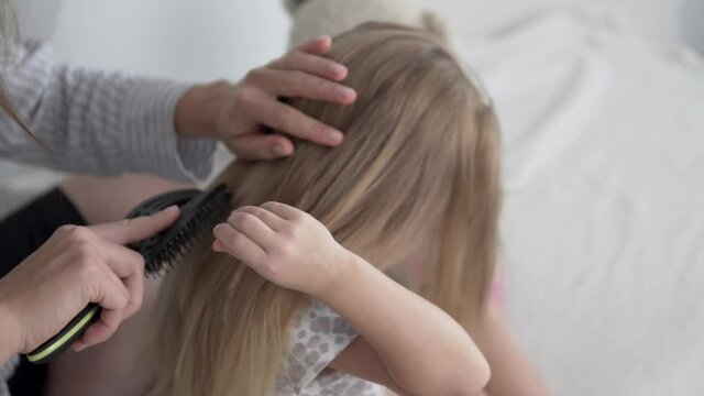 Mom combs the hair of the little daughter's long blonde hair in the morning.