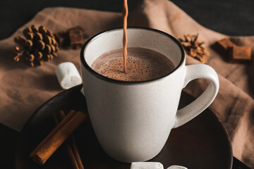 Pouring of hot cocoa drink in cup on table