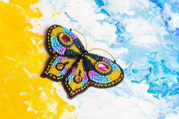 Handmade decoration in the form of a butterfly made of beads on a background of spilled colors.