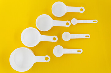 Set of white measuring cups, measuring spoons use in cooking lay on wooden yellow background in top...