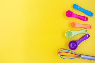 The colorful whisk beside with set of measuring spoon on yellow background with copy space