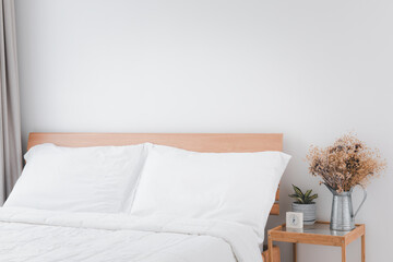 Beautiful white clean cozy bedroom interior with green and dried flowerpot on side wooden table