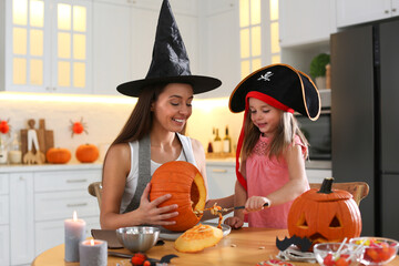Mother and daughter making pumpkin jack o'lantern at table in kitchen. Halloween celebration