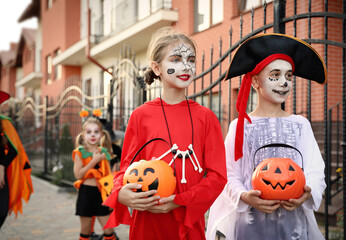 Cute little kids with pumpkin candy buckets wearing Halloween costumes going trick-or-treating outdoors