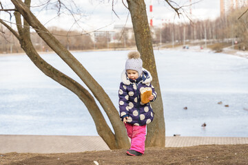 little girl feeds wild prince with bread in winter. frozen pond in the background