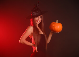 Young woman wearing witch costume with pumpkin on dark  background. Halloween party