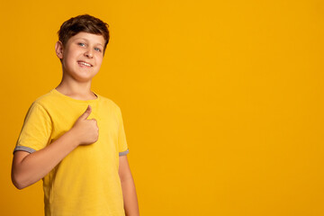 Like gesture. Happy kid. Perfect choice. Encouragement greeting. Portrait of satisfied young boy accepting offer with thumb up smiling isolated on orange empty space promotional background.