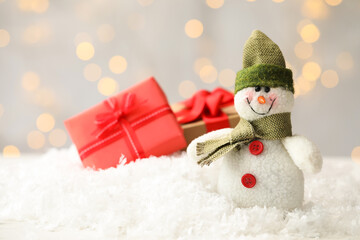 Snowman toy on snow against blurred festive lights, space for text. Christmas decoration