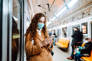 Young woman in a protective mask standing in a subway car with a phone. Protection against viral infections in public transport. Covid-2019.
