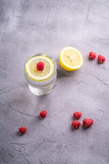 Fresh cold sparkling water drink with lemon, raspberry fruits in glass on stone concrete...