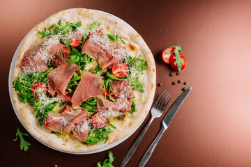 Fresh baked pizza with ham and green herbs on wooden background