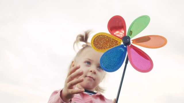 little daughter girl play pinwheel a wind toy lifestyle. happy family concept. child plays with windmill. portrait girl blonde kid holds flower toy spinning pinwheel. happy childhood
