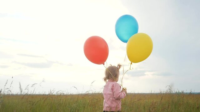 daughter little girl fun runs with balloons a on her birthday outdoors by field. dream happy family concept. child girl kid day. child lifestyle is running and balloons on a background of blue sky