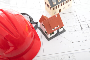 Red hard hat and two small house models on drawings