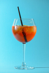 A glass of fruit liqueur in wine glass with a piece of lemon and black plastic straw isolated on pastel blue background.