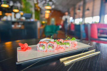 Salmon and caviar sushi rolls served on a traditional plate on a wooden table in a restaurant.