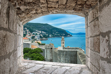 View of Dubrovnik wall, tower and blue sea during sunny summer day from stone window in Dubrovnik, Croatia. Stunning view of Dubrovnik city walls and Dubrovnik old town.