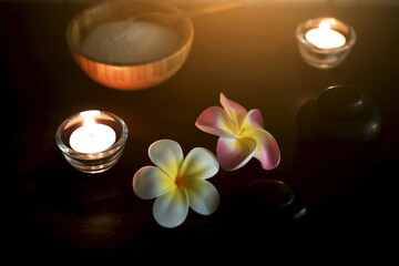 Pink and white Plumeria flowers with rock and Salt for exfoliation in wood Coconut cup on weave plate decoration in spa and Candle light in Glass cup bokeh background.