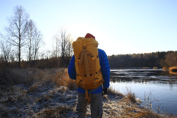 traveler with a backpack by the river / tourist guy on a northern hike, winter trip