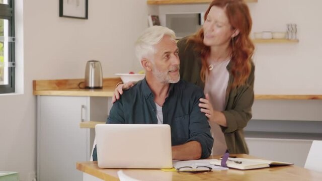 Loving Mature Wife Embracing Husband From Behind While Writing In Book. Happy Middle Aged Couple Making To Do List Of Purchases And Discussing Future Plans. Cheerful Senior Man Working At Home.