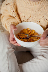 A cute little girl 2 years old in a cozy knitted sweater is having breakfast on the couch. Cozy. Fall.