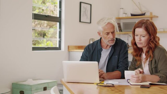 Mature Smiling Couple Sitting And Managing Expenses At Home. Happy Senior Man And Mid Woman Paying Bills And Managing Budget. Middle Aged Couple Checking Accountancy And Bills While Looking At Receipt