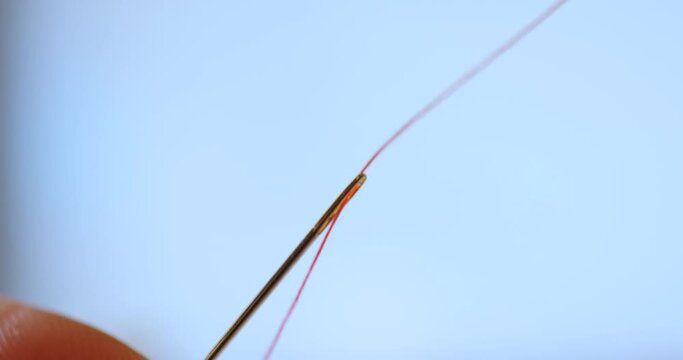 cinematic shot of red thread passing through sewing needle. man sewing project by hand. handmade suit garment with quality thread and fabric. DIY beautiful quilting by fashion creative seamstress