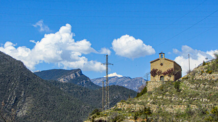 A small chapel on top of the mountain in sunny landscape with electrical towers. Environment concept.