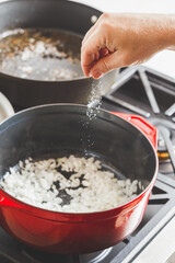 Man's hand putting salt while cooking white onion
