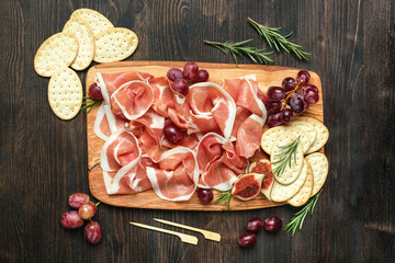 Italian bacon prosciutto crudo or spanish jamon with grapes and crackers on wooden plate. Food for  aperitif and dinner lunch in the restaurant. food delivery home 