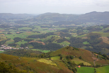 Obraz premium Village in mountains valley with scenic cloudscape. Pyrenees mountains, view from drone. Camino de Santiago landscape. Scenic meadows and agricultural fields in hill valley. Countryside in France. 