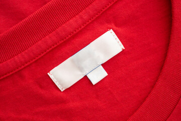 White blank clothing tag label on new red cotton shirt fabric texture background