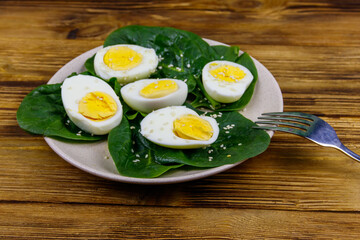 Boiled eggs with fresh spinach leaves and sesame seeds on wooden table