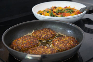 Vegane vegetarische Frikadellen, Fleischklops in einer schwarzen Pfanne mit Gemüse im Hintergrund