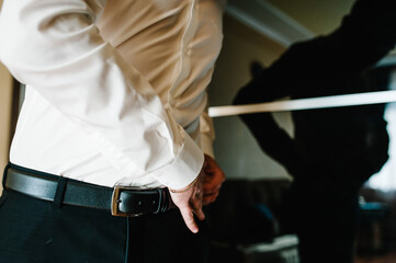 A man in pants and shirt buttoned a leather trouser belt. Groom Dress up a belt with buckle. Businessman wear leather stylish belt. New classic belt.