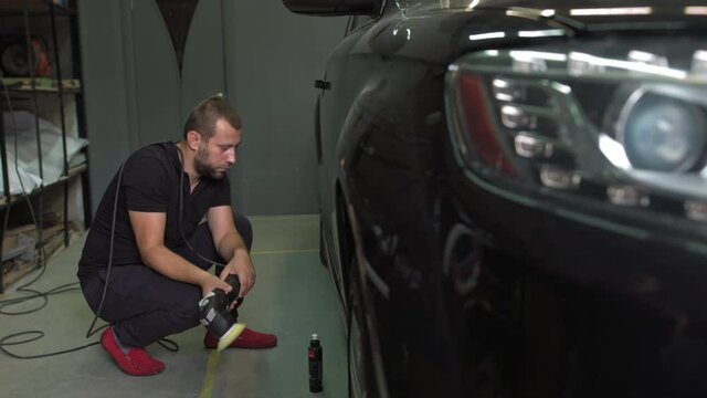Male auto mechanic polishing a black car body with polishing machine for remove scratches. Shot in 4k resolution.Black car, body polishing with polisher in auto service. Waxing car after car wash