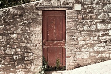 An isolated wooden door of a rural building with stone walls in a downhill street of the medieval village (Gubbio, Umbria, Italy, Europe)