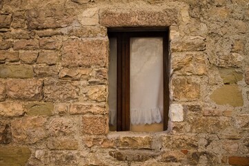 An isolated window with white curtains partially hidden by the stone wall of an abandoned medieval building (Gubbio, Umbria, Italy, Europe)