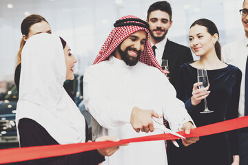 Arab smiles and cuts tape surrounded by colleagues