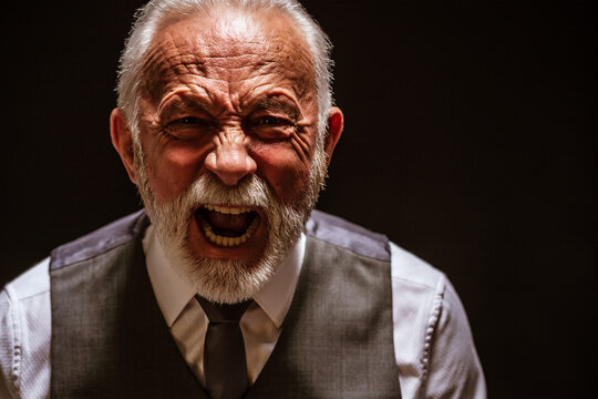 Portrait of furious senior man who is screaming. Black background.