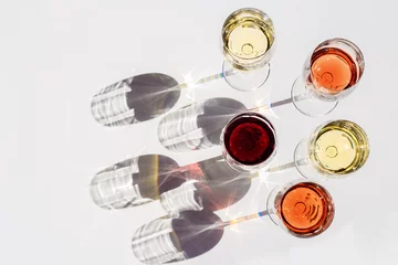 Fototapeten Red, rose and white wine top view in sunlight. Assorted wine in glass on white table. Dark shadows. © yrabota