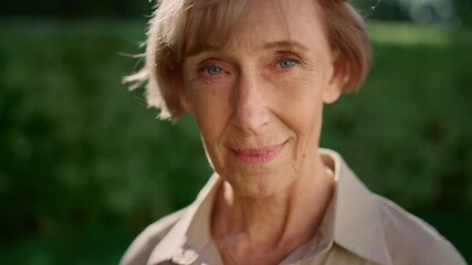 Smiling senior woman posing at camera in summer garden. Senior lady looking down - Powered by Adobe
