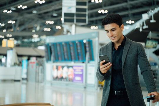 Portrait of young Elegant businessman using mobile phone app check-in boarding pass in airport.Handsome business professional man wearing suit texting smartphone inside office building or terminal