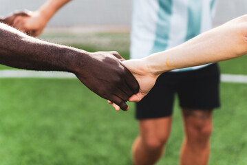 black and white hands holding together in multiethnic group of young people playing football. team of people playing sport, symbol of unifying power and connection of soccer in the field