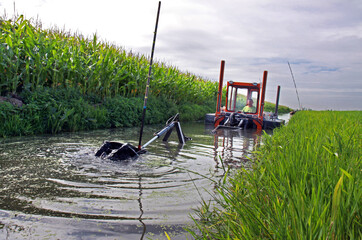 Mini floating suction cutter dredger in operation . The cutter arm cuts the sediment and pumps it...