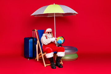 Portrait of his he nice handsome bearded fat Santa tourist sitting in chair holding in hands globe choosing tour destination voyage isolated bright vivid shine vibrant red color background