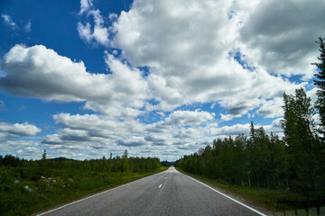 View from relief car windscreen on the blue sky with white clouds, grey asphalt road and landscape with forest and green teeses. Landscape through window