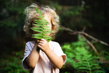 Unrecognizable small child outdoors in summer nature, hiding against fern leaf.