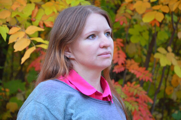 Beautiful elegant woman sits in a park in autumn yellow and red foliage, fall in jeans and a sweater